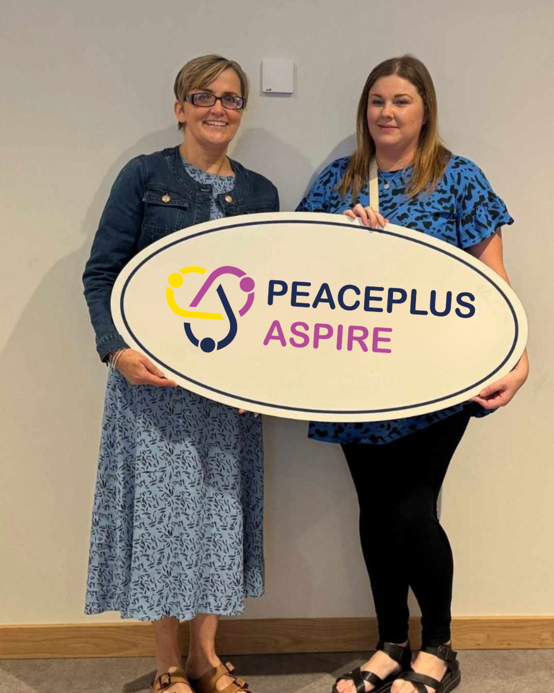 two people holding a peaceplus aspire sign in whilst standing